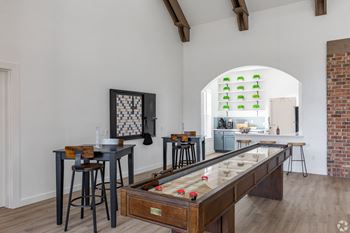 a game room with a shuffleboard table and stools with a brick wall in the background
